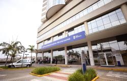 A imagem mostra a fachada do Hospital Metropolitano Dr. Célio de Castro. A foto contém também imagens de palmeiras e uma ambulância estacionada