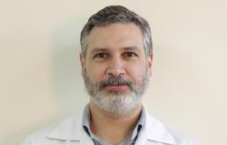 Foto oficial - Leonardo Carvalho da Paixão, Diretor de Planejamento, Diretor Técnico Assistencial, Ensino e Pesquisa do Hospital Odilon Behrens Diretor Técnico Assistencial, Ensino e Pesquisa do Hospital Odilon Behrens - Leonardo Carvalho da Paixão, posa em uma fotografia de rosto em local fechado com camisa tom de azul claro e jaleco de cor branca.