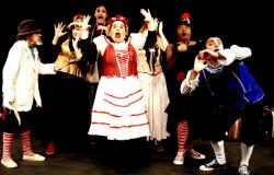 Sete atores, com maquiagem branca e roupas ao estilo medieval e circense, fazem expressões de espanto. 