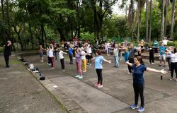 A foto mostra um grupo de pessoas reunidas em um parque, fazendo aula de Lian Gong, que é uma prática corporal chinesa. 