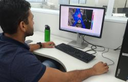 Homem, sentado em frete a computador, vê simulação de impactos ambientais na tela. 