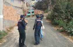 Dois técnicos da Defesa Civil acompanham cidadão em vila, mais à frente, outros dois técnicos caminham. Foto ilustrativa.