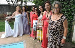 Mulheres posam para foto usando vestidos longos, ao lado de uma piscina