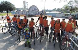 Doze alunos e uma criança, cada um com sua bicicleta, na frente da Igrejinha da Pampulha, durante o dia. 