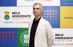 Homem grisalho, em pé, com as mãos para trás, usando camisa preta e paletó branco.