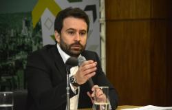 Foto oficial - Bruno Passeli, Subsecretário de Planejamento e Orçamento e Secretário Adjunto da SMPOG Subsecretário de Planejamento e Orçamento e Secretário Adjunto da SMPOG - Bruno Passeli, posa em uma fotografia em local fechado com terno de tom escuro e camisa branca segurando um microfone.