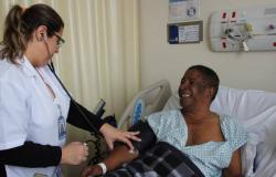 Profissional de saúde afere pressão de cidadão em leito de hospital.