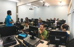 Homem dá aula a cerca de dez alunos, sentados em frente a seus computadores. 