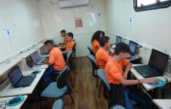 Seis crianças de camiseta laranja usam os computadores da carreta do Projeto Conexão Aberta.