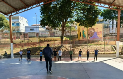 meninos em uma quadra de futebol coberta, todos em uma linha horizontal de frente para um adulto, que está de costas para a foto. 