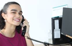 Jovem branca com blusa vermelha na frente do computador segurando um telefone 