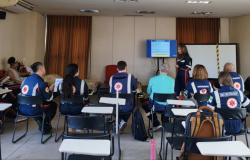 A foto mostra um ambiente interno, com pessoas participando de treinamento. 