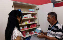 Homem segura antibiótico em frente a armário de medicamentos, ao lado de mulher. 