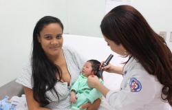 Mãe sefura bebê enquanto técnica de saúde faz teste da orelha. 