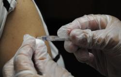 Mão enluvada aplica, com injeção, vacina em braço humano. 