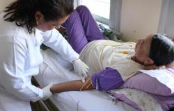 Médica checa braço de paciente, que está deitada. 