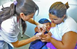 Criança, no colo da mãe, recebe vacina por uma enfermeira