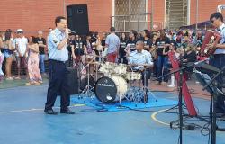 Cantor e baterista da Banda da Guarda Municipal se apresenta em quadra esportiva; ao fundo, plateia com mais de 60 pessoas. 