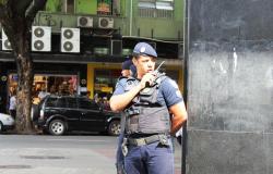 Guarda municipal, em esquina de uma rua, fala com rádio preso ao ao ombro, durante o dia.