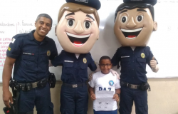 Guarda Municipal, estudante e dois guardas com máscaras humanas de guarda municipal similares a desenho animado, posam para foto. 