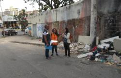 Três pessoas usando colete conversam ao lado de lixo irregular 