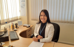 Mulher vestindo blazer claro, sentada em uma mesa de escritório