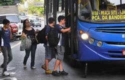 Dois estudantes entram em ônibus coletivo, durante o dia.