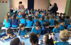 Crianças sentadas em uma mesa para receber alimentação em escola infantil