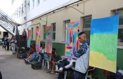 Homens e mulheres ao lado de painéis coloridos no aniversário do Centro Especializado para População em Situação de Rua.