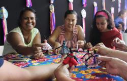 Quatro mulheres mostram as bonequinhas negras - abayomis - em cima da mesa com forro colorido. 