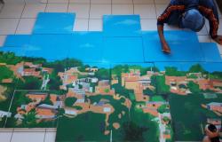 Jovem pinta favela em módulos quadrados no chão. 