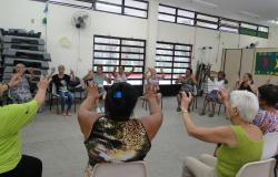 Mais de doze adultos, sentados em cadeiras dispostas em forma de círculo e com as mãos para cima, participam de dinâmica pela saúde no Cras Mariano de Abreu. 
