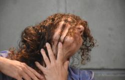 Mulher com o rosto coberto pelo cabelo ruivo levemente inclinado para trás com as mão apoiadas no pescoço e colo. 