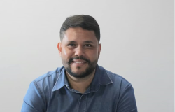 Homem branco de barba e bigode, veste camisa azul e sorri para a foto