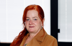 Mulher branca de cabelos longos ruivos e lisos veste casaco marrom claro