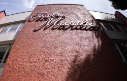 Fachada do teatro vista de baixo para cima, com parede de textura avermelhada e a inscrição em "Teatro Marília" em destaque no topo