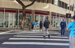 Pedestres atravessam a via na faixa de pedestres com o sinal verde.