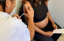 A foto mostra uma gestante recebendo uma vacina no braço aplicada por uma profissional de saúde. 