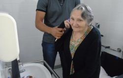 Paciente idosa treina movimentos cotidianos em frente a uma pia, auxiliada por técnico do Centro de Reabilitação de Venda Nova.