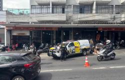 Uma viatura da Guarda Municipal de Belo Horizonte encontra-se estacionada em frente a um estabelecimento comercial, com agentes ao redor e materiais da blitz educativa posicionados na viatura. A circulação do trânsito no local é orientada por cones de sinalização, enquanto carros e motocicletas transitam ao redor.