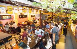 Cerca de 30 jovens e adultos bebem cerveja e conversam em mesas de bar à tarde. Foto: Divulgação
