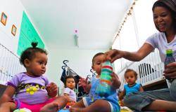 Educadora onfantil interage com quatro crianças com menos de um ano de idade com chocalho e brinquedos feitos como material reciclável. 