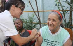 Agente de saúde aplica vacina no braço direito de uma idosa durante visita no Centro de Saúde Salgado Filho