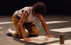 Criança ajoelhada com as mãos no chão olha para papel em branco; cena da peça infantil "O Pequeno". Foto: Filipe Hott