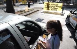 No primeiro plano, uma menina, aluna da rede municipal de ensino, entrega panfleto em carro. Ao fundo, dois alunos seguram uma faixa, em cima da faixa de pedestre, com os seguintes dizeres: "Maio amarelo: eu sou + um lutando por um trânsito mais humano".