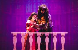 Bela, jovem com trajes de princesa, lê livro junto à Fera em uma sacada em cena teatral.