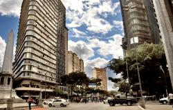 Praça Sete de Setembro, com monumento à esquerda, prédios altos dos lados e ao centro, movimento de carros e pessoas no cruzamento das avenidas Amazonas e Afonso Pena.