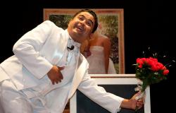 Marcelo Ricco, em cena, segurando um buquê em frente a fotos de casamento.
