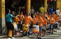 Crianças com camisetas cor laranja com instrumentos de percussão em frente à entrada Shopping Caetés