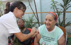 Profissional de saúde aplica vacina em braço direito de idosa do Centro de Saúde Salgado Filho
